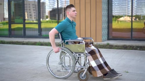 Young Man in a Wheelchair. A Man Rides in a Wheelchair Against the Background of a Glass Building