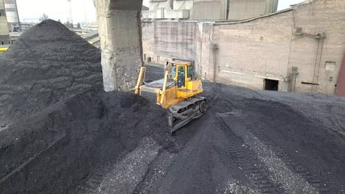 Bulldozer-Traktor sammelt schwarze Kohle auf dem Versorgungsfeld des thermoelektrischen Kraftwerks.