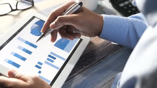 Rear View of Man Hand with Pen Analyzing Charts on Digital Tablet