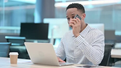 Young Adult Man Talking on Phone at Desk