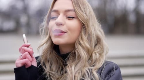 Mujer rubia vapeando en la calle