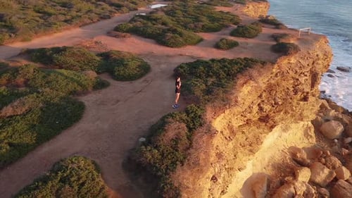 Woman Pauses on Ocean Cliff at Sunset