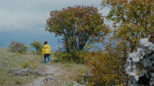Lonely boy in a yellow jacket is walking along a path in nature.