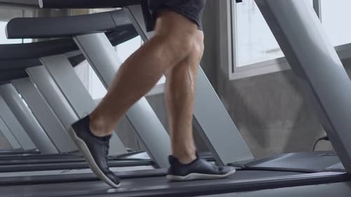 Muscular shirtless man running on treadmill at the gym