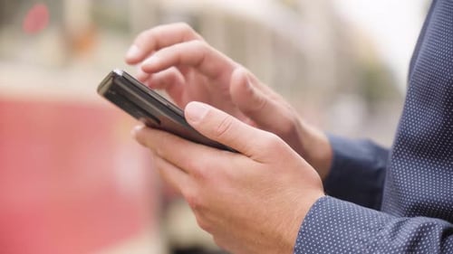 A Man Works on a Smartphone in an Urban Area Closeup a Street in the Blurry Background