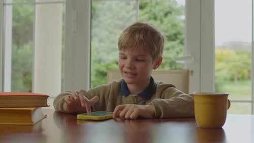 School Boy Playing Video Games Using Mobile Phone Sitting at Home By the Window