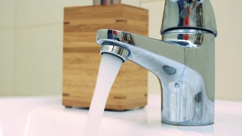 Water Pours Out of a Faucet in a Bathroom - Closeup
