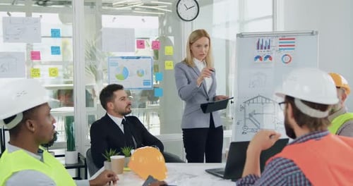 Una gerente femenina da instrucciones de trabajo a un equipo profesional diverso de constructores durante la reunión