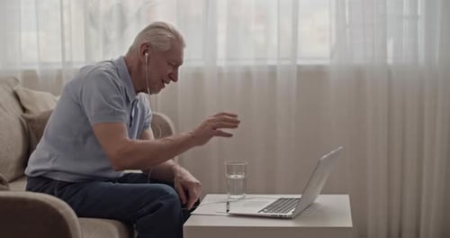 Senior Man Talking on Laptop with Earphones at Home