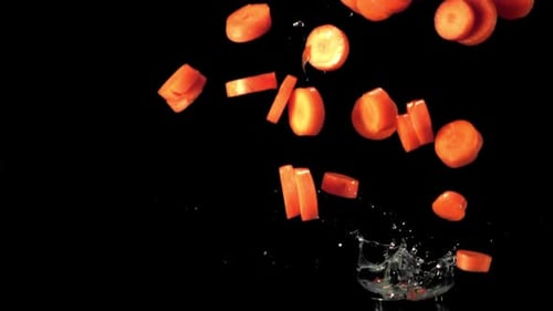 Superzeitlupen-Karottenstücke fallen mit Spritzern ins Wasser