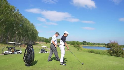 4K Asian senior man teaching his adult son hitting golf ball on golf course.