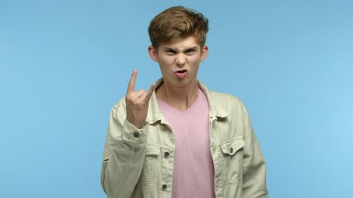 Junger begeisterter Typ im lässigen Outfit genießt das Konzert und zeigt Rocknroll-Hörner, Gestik und Zittern