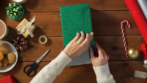 Hands Wrapping Christmas Present on Wooden Table