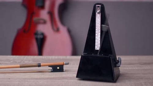 Swinging Black Metronome on Wood Table with Violin