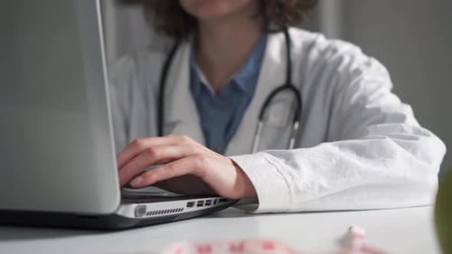 El médico está escribiendo en una computadora portátil. Las manos del médico trabajan escribiendo