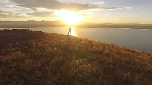 Flying towards man overlooking lake at sunset in golden landscape