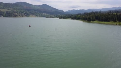 Luftaufnahme des Sees mit einer in der Mitte schwebenden Struktur und Bergen im Hintergrund