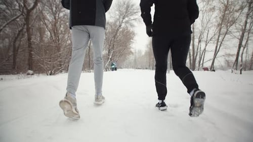 Man and Woman Running Along a Snow Road in the Park
