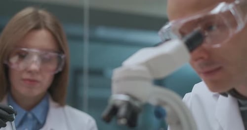 Equipe de jovens cientistas está trabalhando em laboratório farmacêutico, mulher está explorando reagentes e