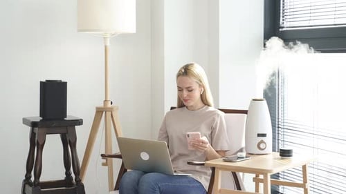 Woman Using Laptop and Phone at Home