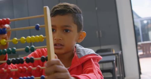 Vista frontal de un colegial asiático resolviendo un problema matemático con un ábaco en el escritorio de un aula de la escuela 4k