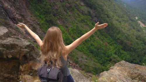 Young Woman-traveler with a Backpack in the Mountains. She Is Looking at the Majestic Valley Down