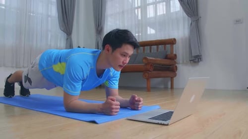 Man Doing A Plank While Watching Online Tutorial On Laptop, Exercising In Living Room