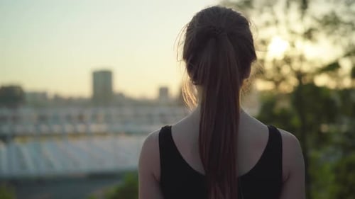 Back View of Brunette Woman Walking To Blurred Urban City Along Park at Sunset. Positive Caucasian