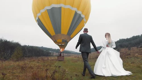 Newlyweds Walking to Hot Air Balloon in Rural Field