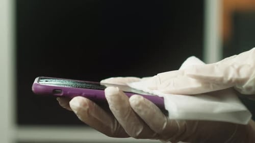 Gloved Hands Disinfecting Purple Smartphone with Wipe