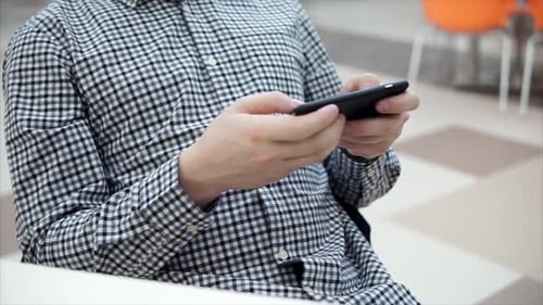 Vue rapprochée d'un homme jouant sur un smartphone dans un café.