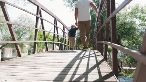 Father and His Little Son Walking on the Bridge Above the River