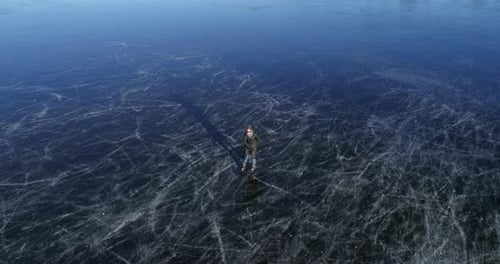 Slow motion aerial view of woman iceskating on frozen lake
