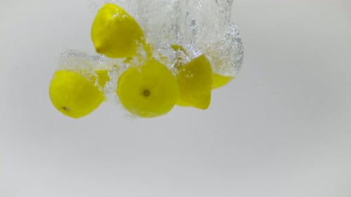 Bright Yellow Lemons Splashing into Clear Water