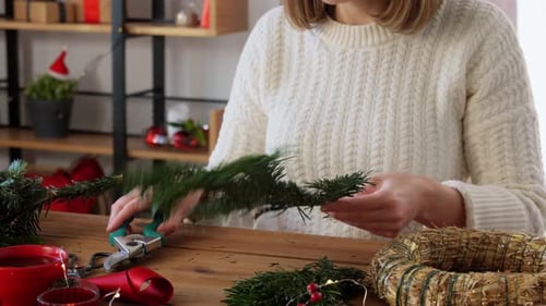 Woman Crafts Christmas Wreath with Evergreens at Table