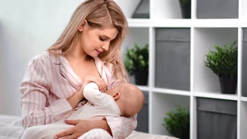 Blonde Woman Breastfeeding Newborn Baby Indoors