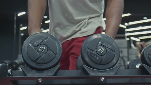Close Up of Afro Man Takes and Lifts Two Dumbbells in Gym
