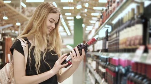 Woman Examines Bottle of Wine in Supermarket Aisle
