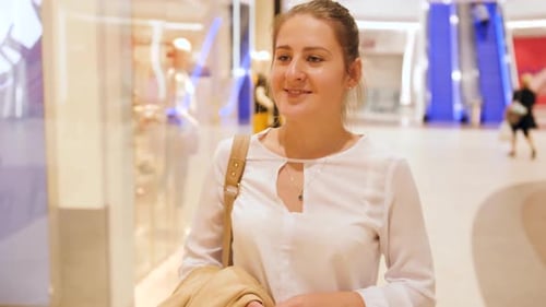 Video of Smiling Young Woman Walking in the Hall at Big Shopping Mall and Looking on Clothes Behind
