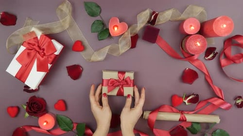 Female hands are tying red ribbon bow on wrapped gift box for St. Valentine's Day
