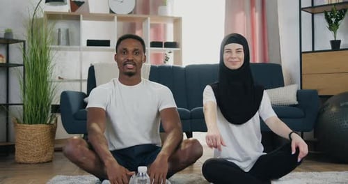 Couple assis dans un lotus posant sur le sol dans une chambre joliment décorée et montrant les pouces en l'air