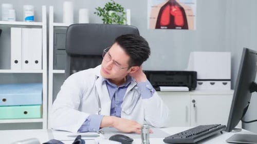 Stressed and overworked Asian male doctor sitting on table in hospital.