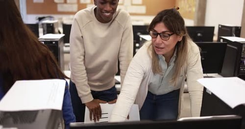 Mature teacher working with multiracial students inside computer classroom at university