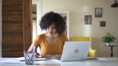 Woman Working at Home with Laptop and Notebook
