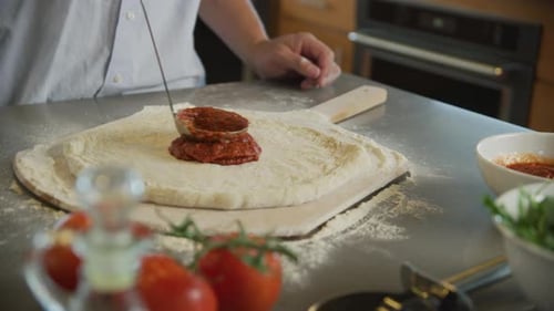 Applying Tomato Sauce To Pizza Dough In Kitchen