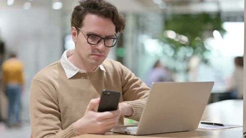 Young Adult Using Laptop and Mobile Phone at Desk