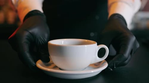 The Waiter in the Restaurant Puts a White Cup of Hot Coffee or Tea in Front of the Camera or in