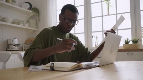 Young Adult Working at Table with Laptop and Notebook