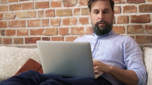 Bearded Man Types on Laptop Computer at Home
