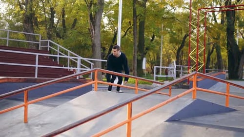 Young Extreme Skateboarder Listening to the Music in Earphones Grinding Down Rail in the Skatepark